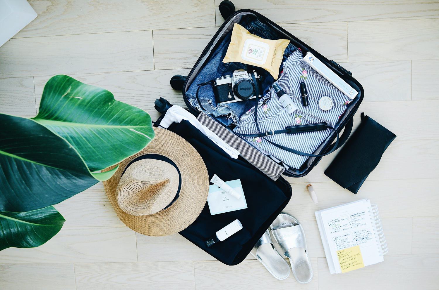 Open luggage on floor with hat and camera