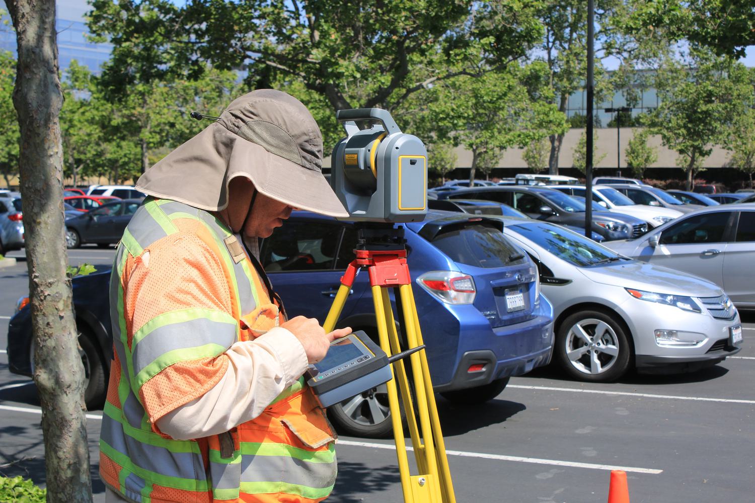 Guy in car park looking at land survey equipment