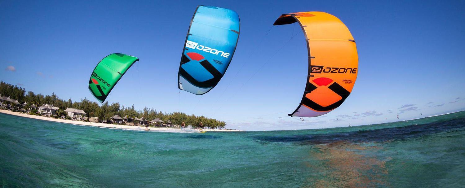 Three bright kitesurf sails close up with shoreline in the background