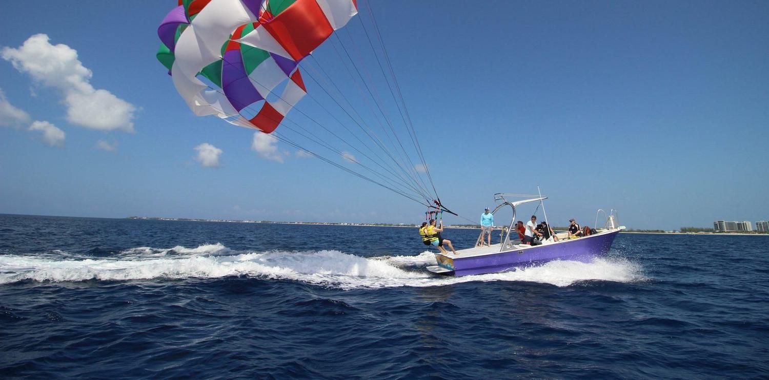 Two people starting to lift off parasailing behind a boat