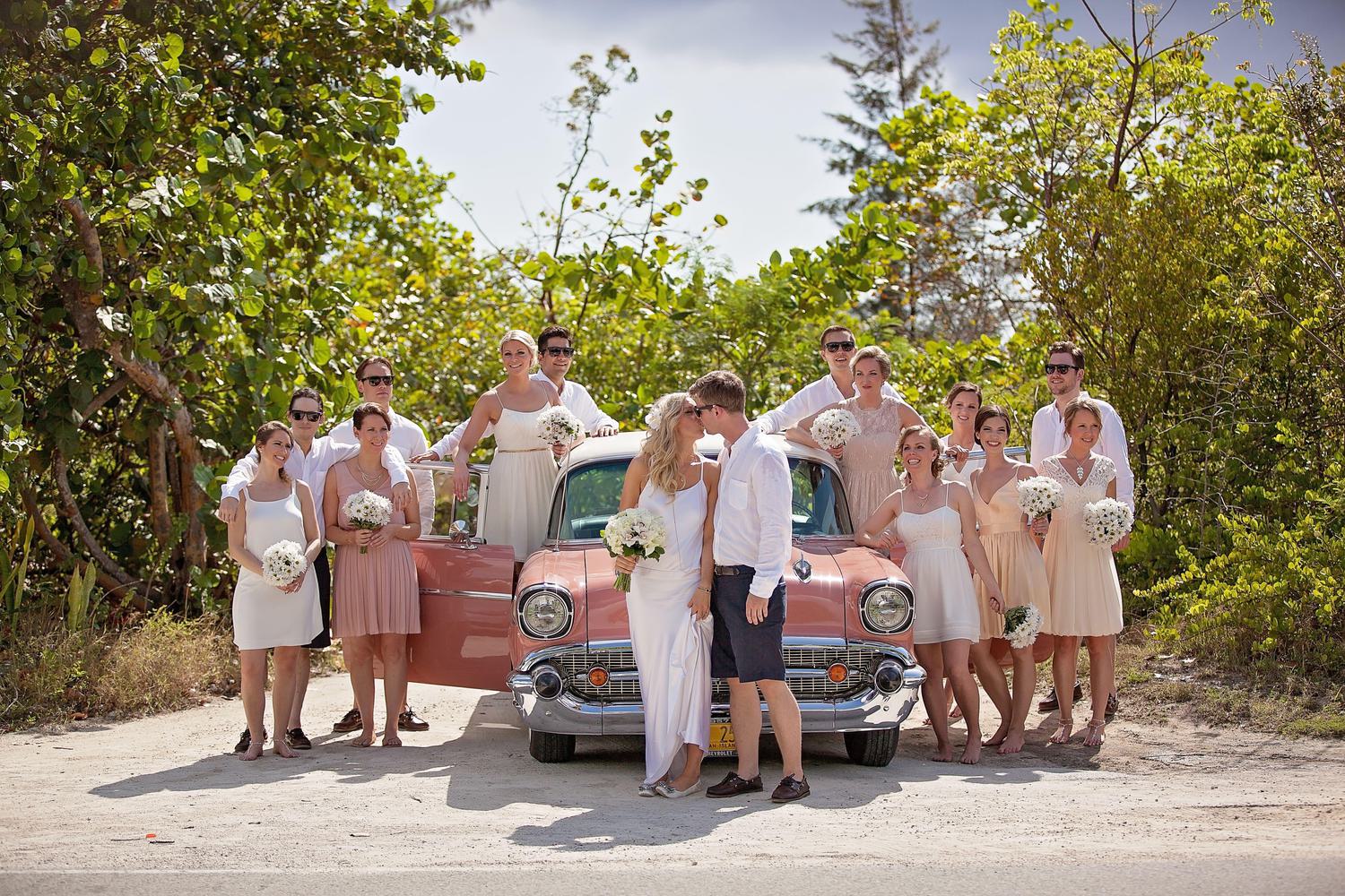 Wedding party sitting in front of pink classic car