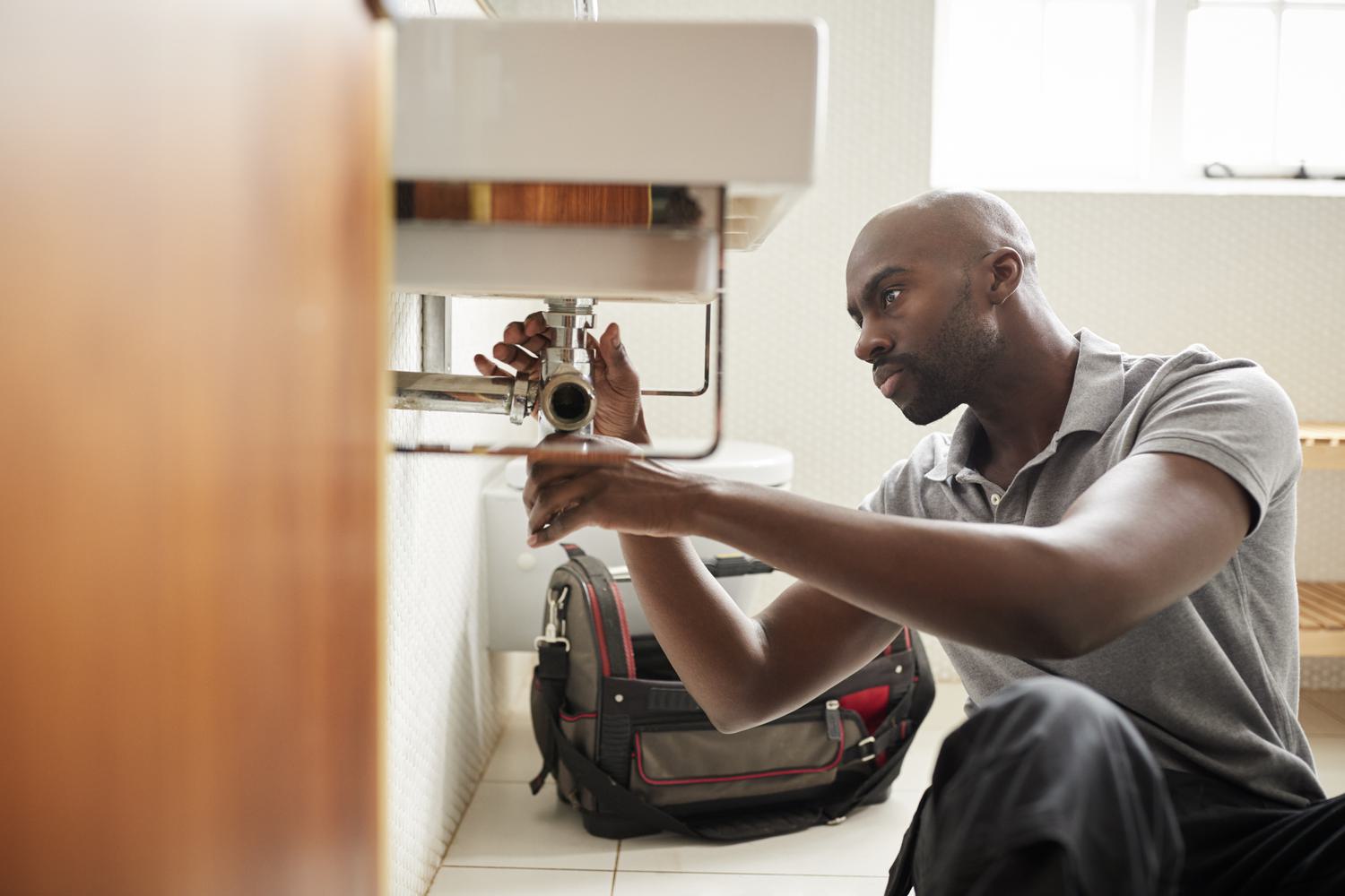 Young black male plumber fixing under sink