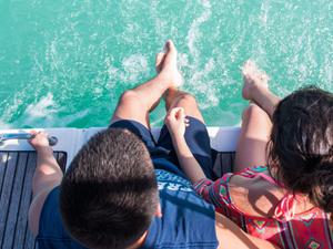 Couple sitting with feet hanging in the water off the edge of a boat