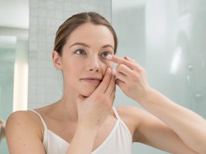 Woman Holding contact lens to eye looking in mirror