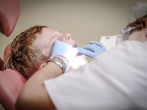Blonde child sitting in dentist armchair getting teeth cleaned
