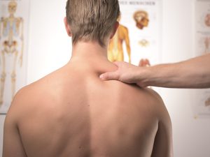 Chiropractor squeezing mans shoulder looking at charts