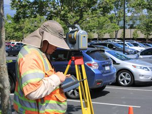 Guy in car park looking at land survey equipment