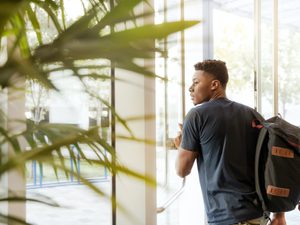 Man looking outside window carrying black and brown backpack