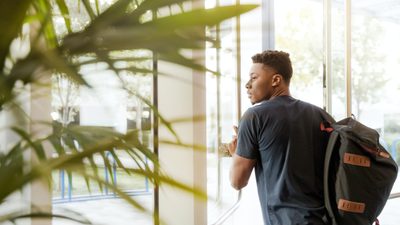 Man looking outside window carrying black and brown backpack