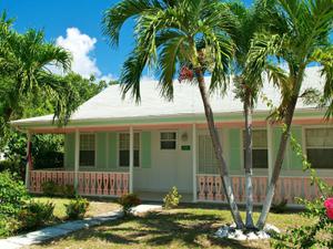 Quaint mint green traditional cayman cottage with veranda and pink blossom trees