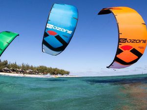 Three bright kitesurf sails close up with shoreline in the background