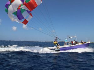 Two people starting to lift off parasailing behind a boat