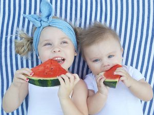 Two young children eating watermelon on a striped blanket
