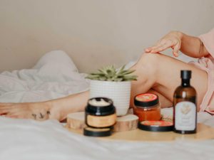 Woman with holistic beauty products lounging on a bed with only leg visable