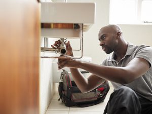 Young black male plumber fixing under sink