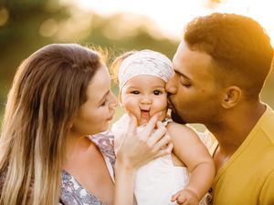 Young parents squeezing chubby newborn cheeks